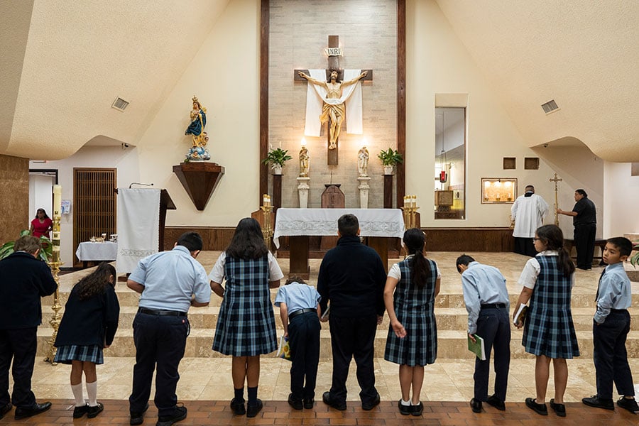 All Saints students bow and make the sign of the cross before the altar at All Saints Church during a school Mass on May 17, 2023.